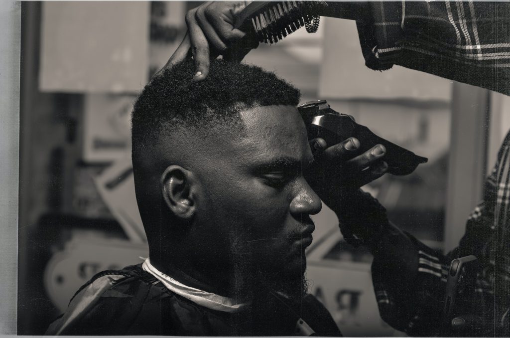 Black and white image of a black man getting a haircut at a barbershop. Credit: BariKive from Pexels.