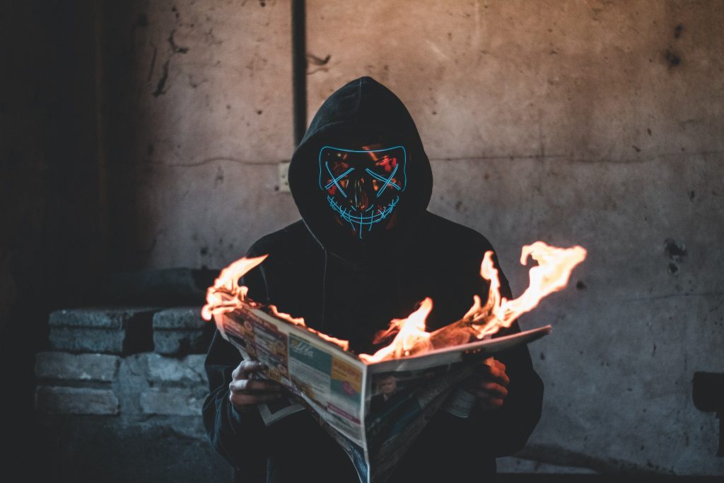 Man with LED mask reading a burning newspaper. Photo by Connor Danylenko from Pexels.